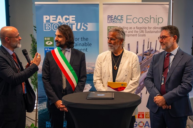 Officials at a ceremony in front of Peace Boat US banners