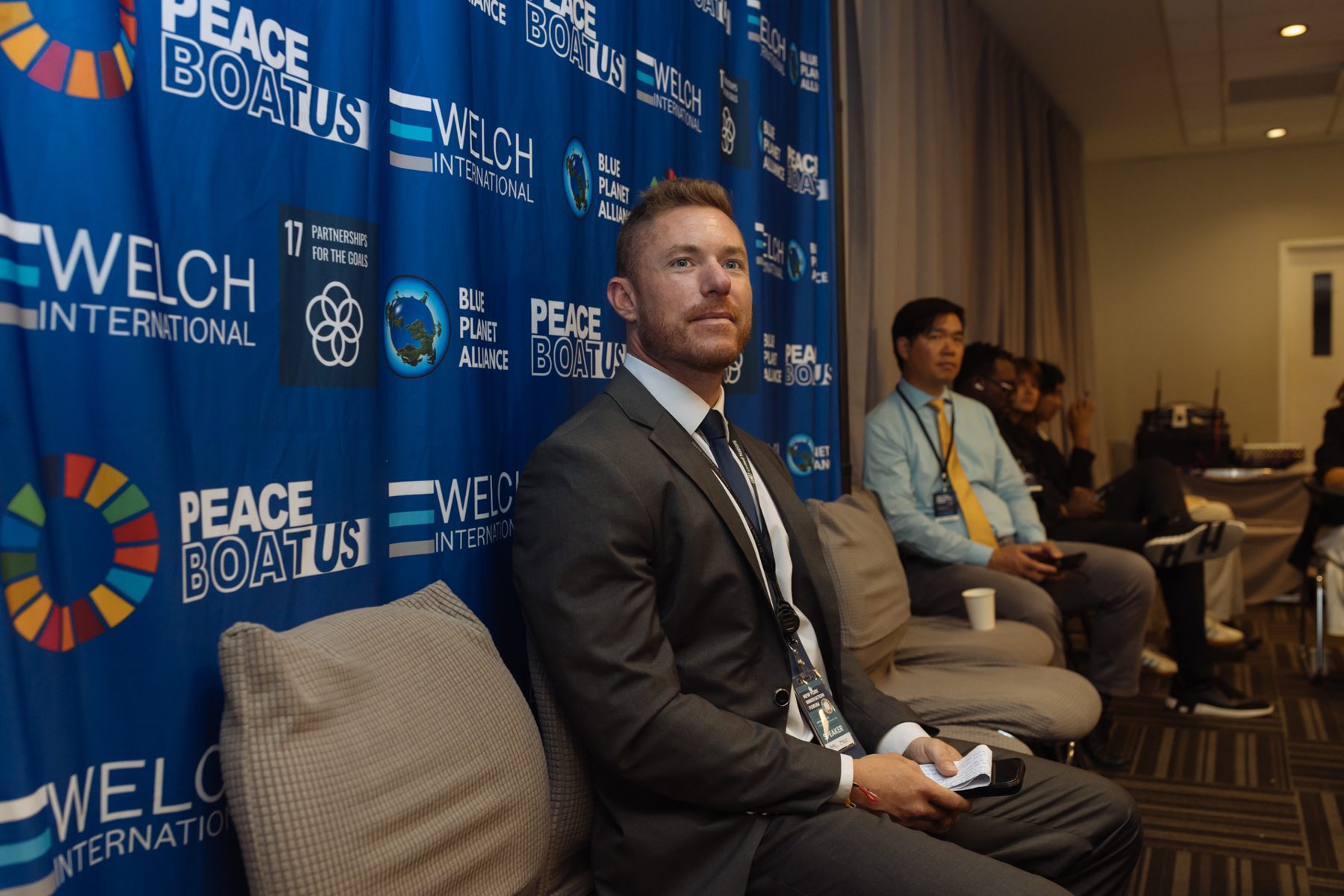 Speaker seated in front of a Welch International press wall